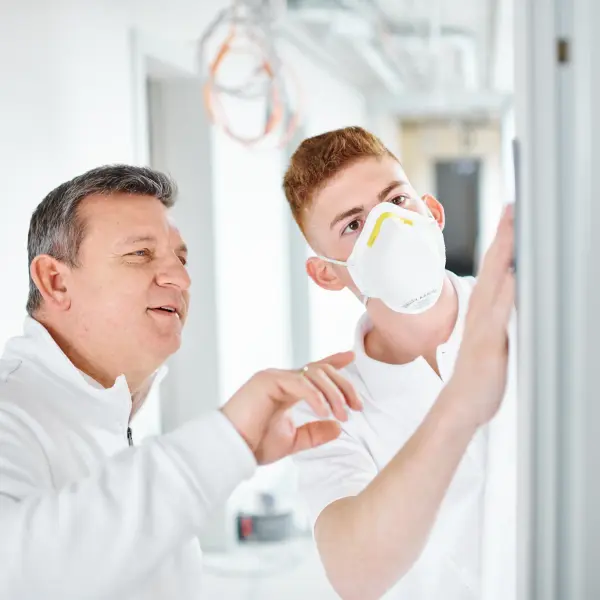 Maler zeigt einem Auszubildenden wie er etwas an der Wand machen soll