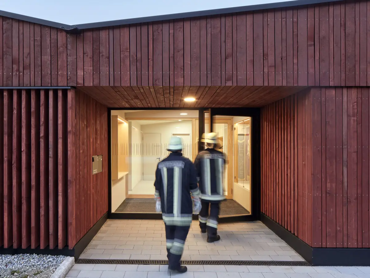 Zwei Feuerwehrmänner gehen in das rote Gebäude