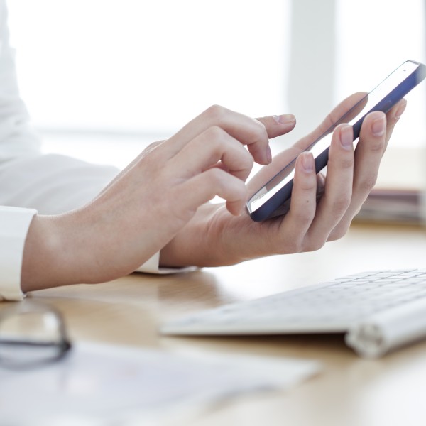 Hand tippt in ein Handy und sitzt am Schreibtisch