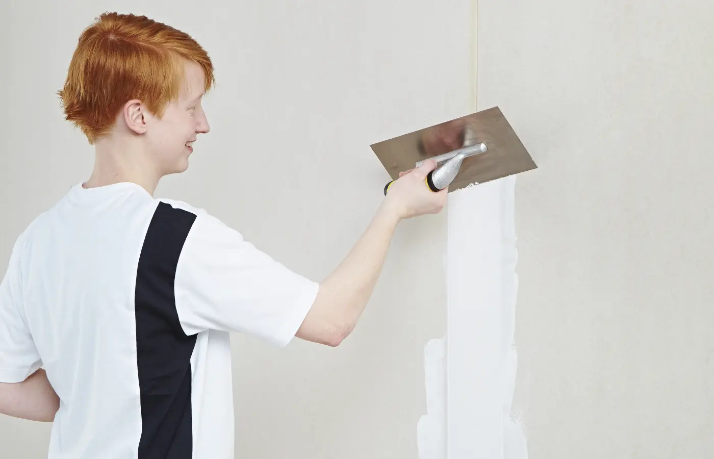 Handwerkerin arbeitet mit Spachtel an der Wand 
