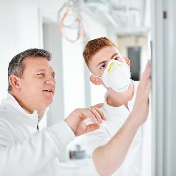 Meister erklärt jungem Mann etwas an der Wand