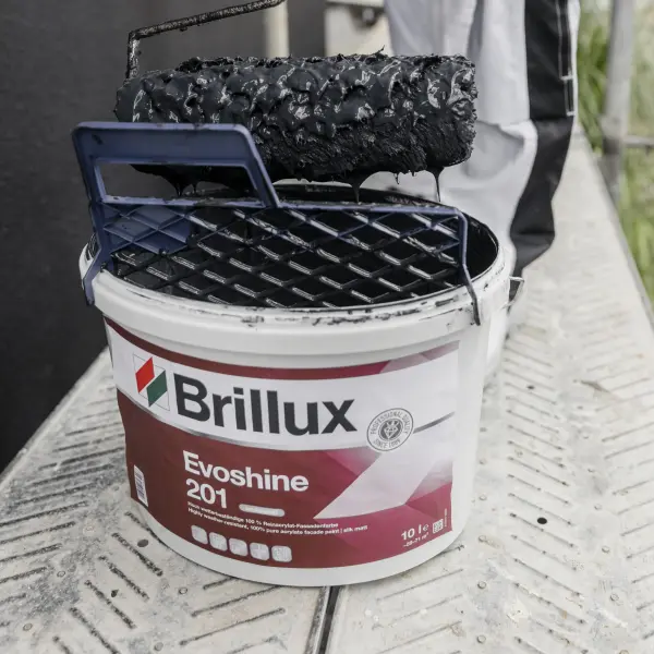 Ein Evoshine Farbeimer steht auf einer Baustelle und wird von einem Maler benutzt indem er eine Rolle eintaucht.
