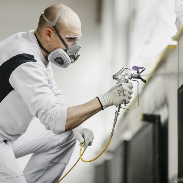 Maler mit Maske sprüht mit einem Sprühgerät Lack an einen Türrahmen