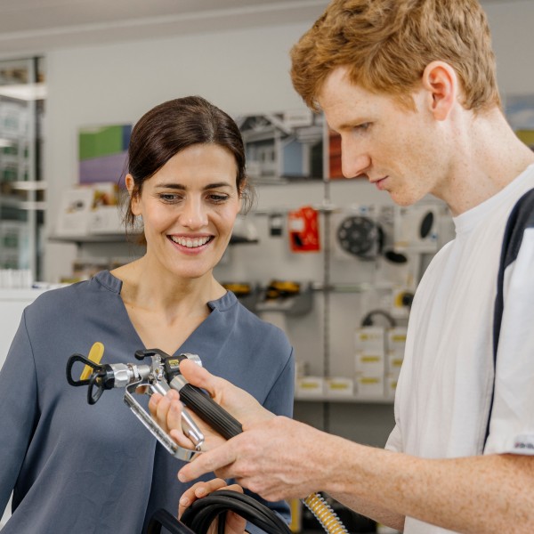 Eine Niederlassungsmitarbeiterin erklärt einem Maler ein Spritzgerät