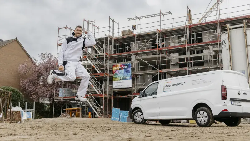 Maler springt vor dem Firmenauto in die Höhe
