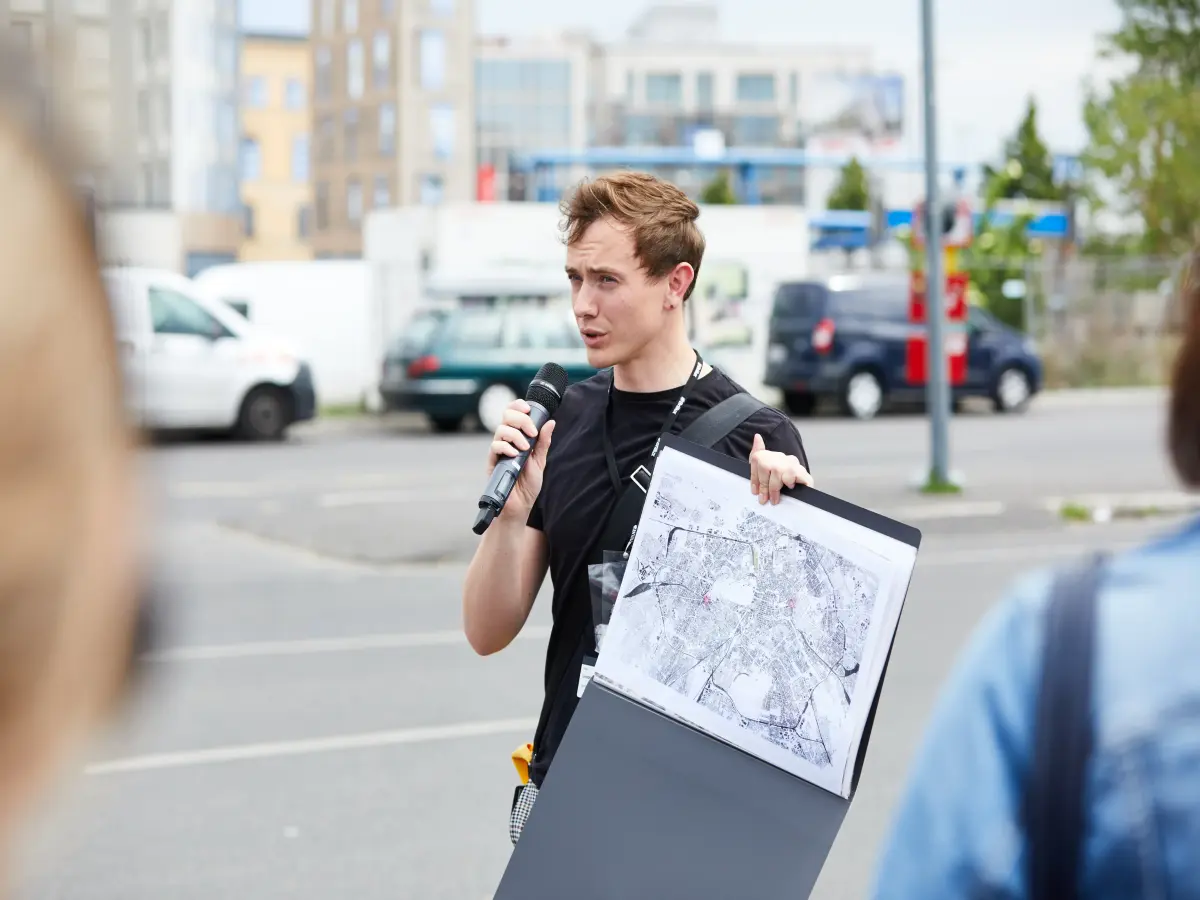 Berlin: Person mit Mikrofon erklärt etwas und zeigt eine Karte