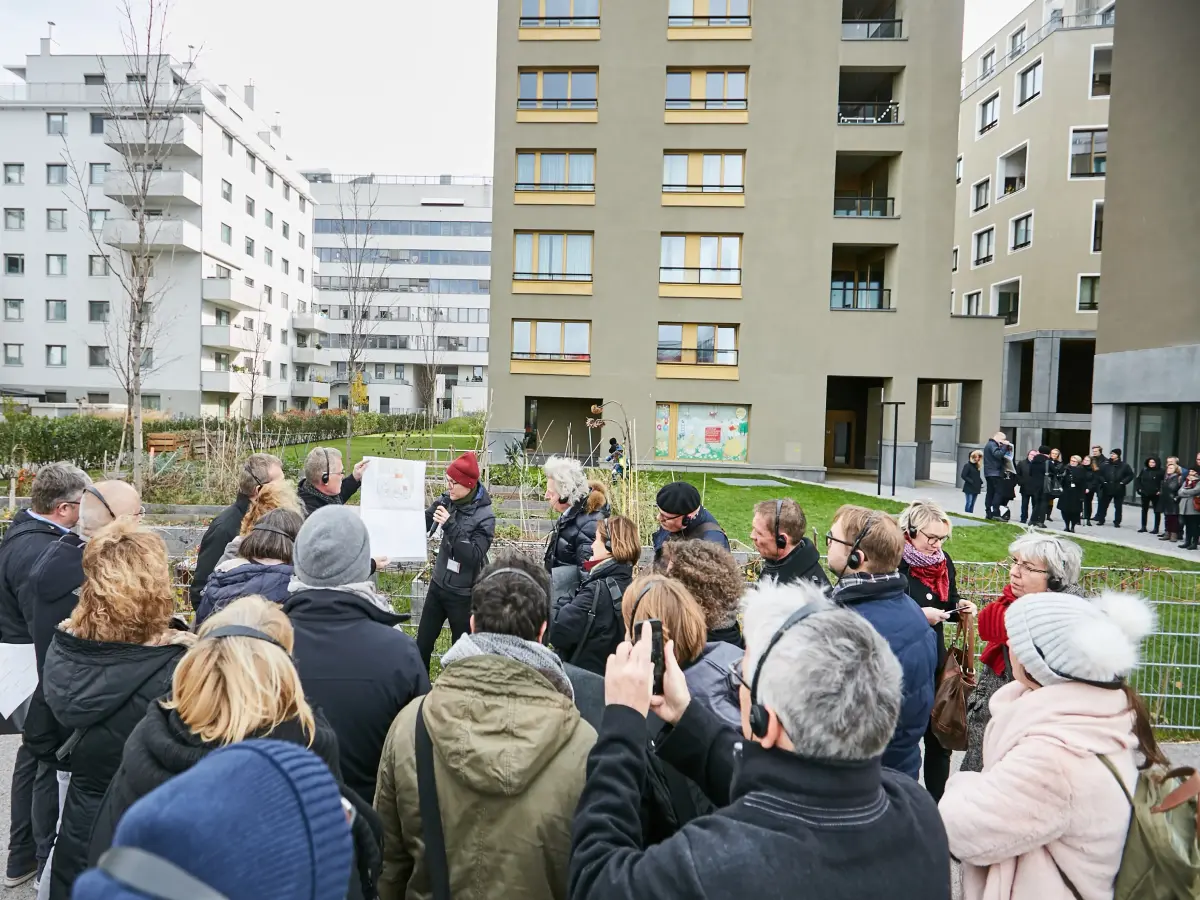 Wien: Menschen stehen draußen vor einem Gebäude und hören einer Person zu, die etwas vorträgt.