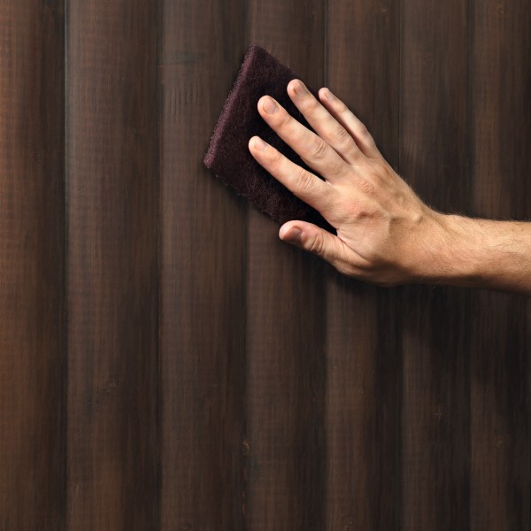 Eine Hand schleif eine braune Holzwand ab