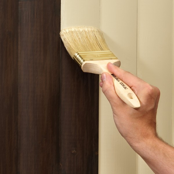 Eine Hand streicht Lasur auf eine braune Holzwand