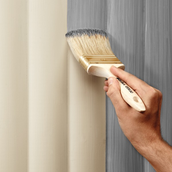Eine Hand streicht eine bereits lasierte Holzfläche von beige in grau