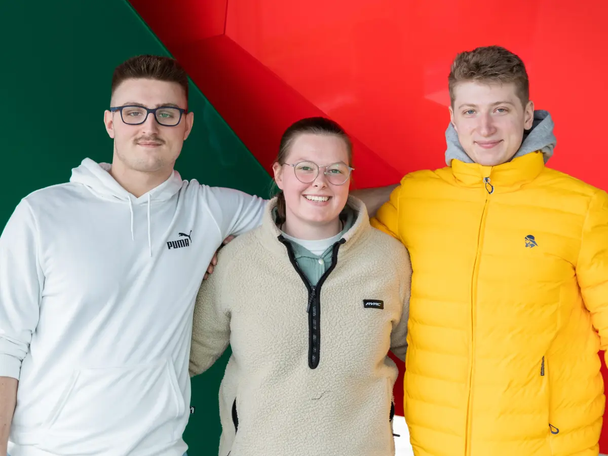 Porträtbild von drei Personen, die sich umarmen und in sie Kamera schauen