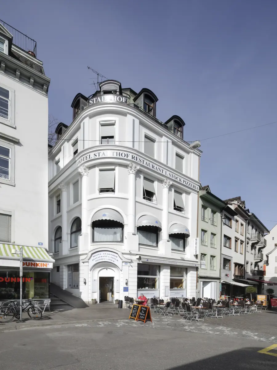 Weißes dreistöckiges Restaurant an gepflastertem Platz.