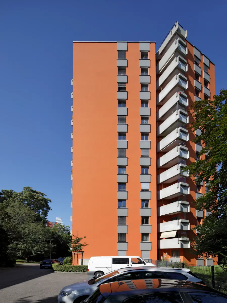 Blick von unten auf ein orangefarbenes Hochhaus mit Balkonen vor blauem Himmel.