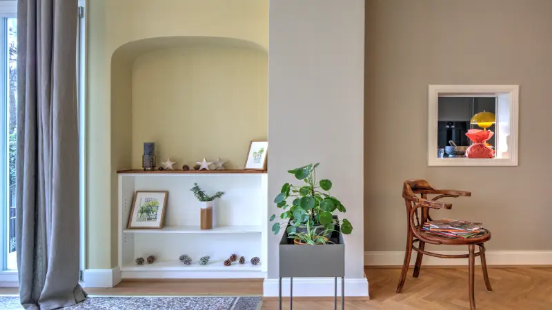 Ein heller Raum mit dekorativem Wandregal, Pflanze, Holzstuhl und ruhigen Farbtönen.