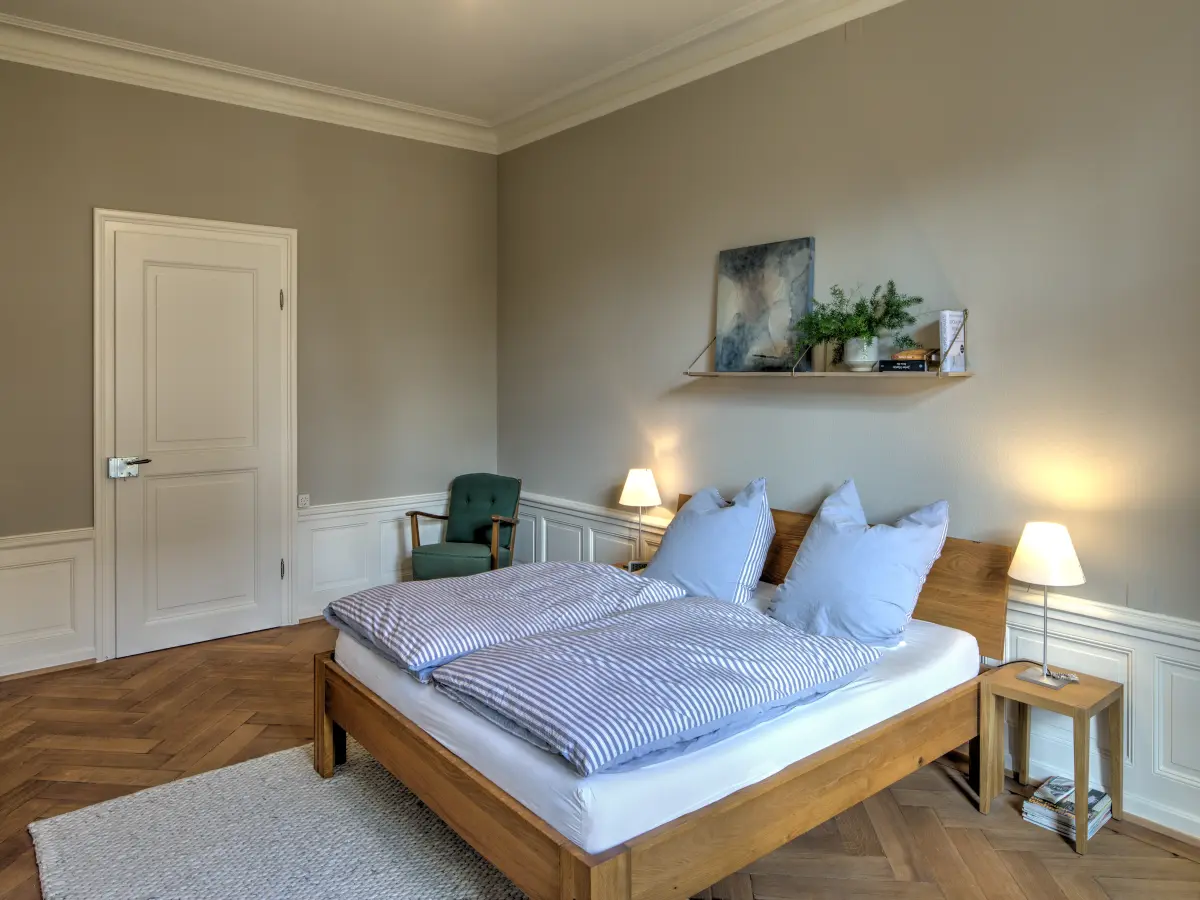 Helles und gemütliches Schlafzimmer mit modernem Holzbett, dezenten Wandfarben, stilvollen Nachttischlampen und einem Wandregal mit Dekoration.