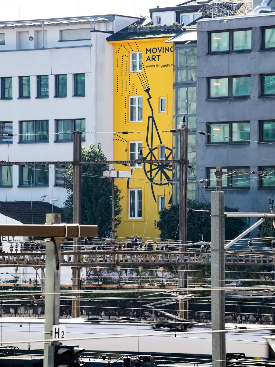 Gelbes Gebäude mit Kunstwerk und Schriftzug "MOVING ART" nahe den Bahngleisen, in der Nähe des Museums Tinguely in Basel.
