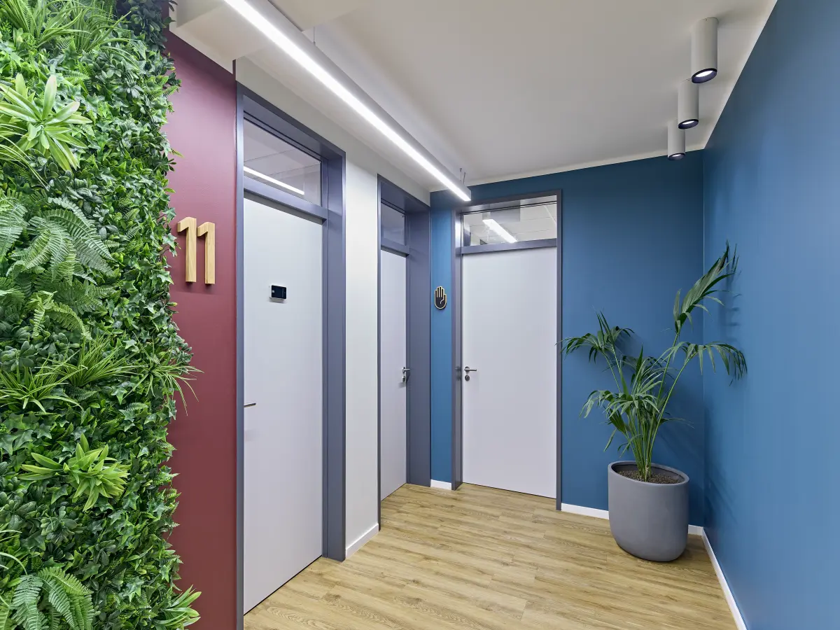 Flur einer Praxis mit Pflanzenwand, nummerierter Tür und großer Topfpflanze.