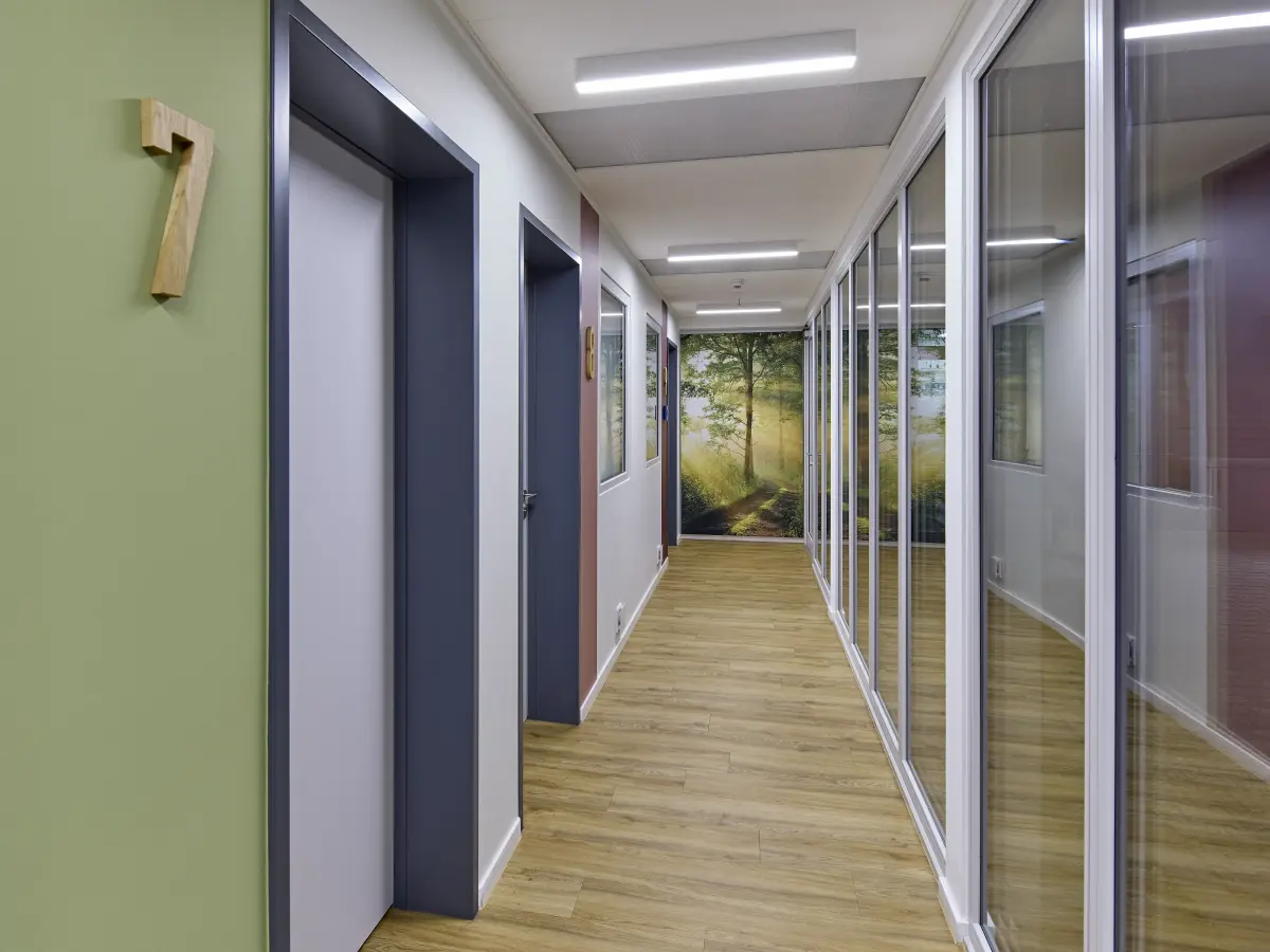 Heller Praxisflur mit nummerierten Türen und großem Waldmotiv am Ende des Gangs.