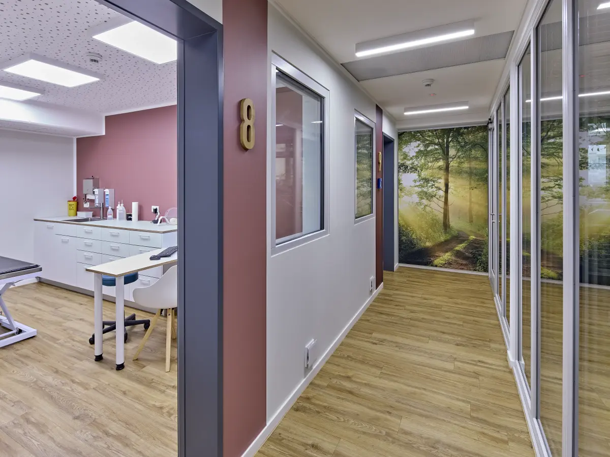 Moderner Praxisflur mit Untersuchungsraum und Waldmotiv an der Wand.