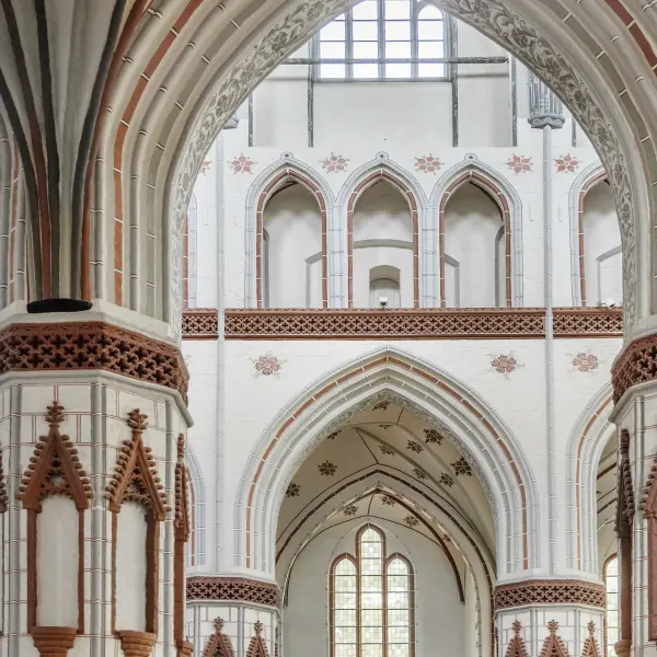  Innenansicht einer Kirche mit hellen, weiß verputzten Wänden und kontrastierenden, verzierten roten Backsteinbögen und Säulen.