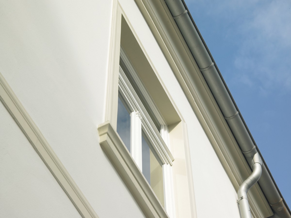 Nahaufnahme der weißen Fassadenleiste und der Traufe eines Hauses vor blauem Himmel.