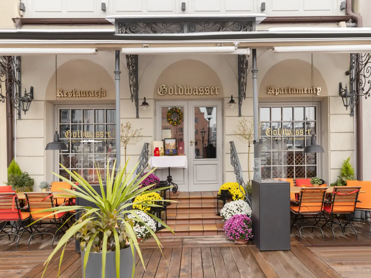 Eleganckie wejście do restauracji z tarasem, napisem Goldwasser i miejscami do siedzenia na zewnątrz.
