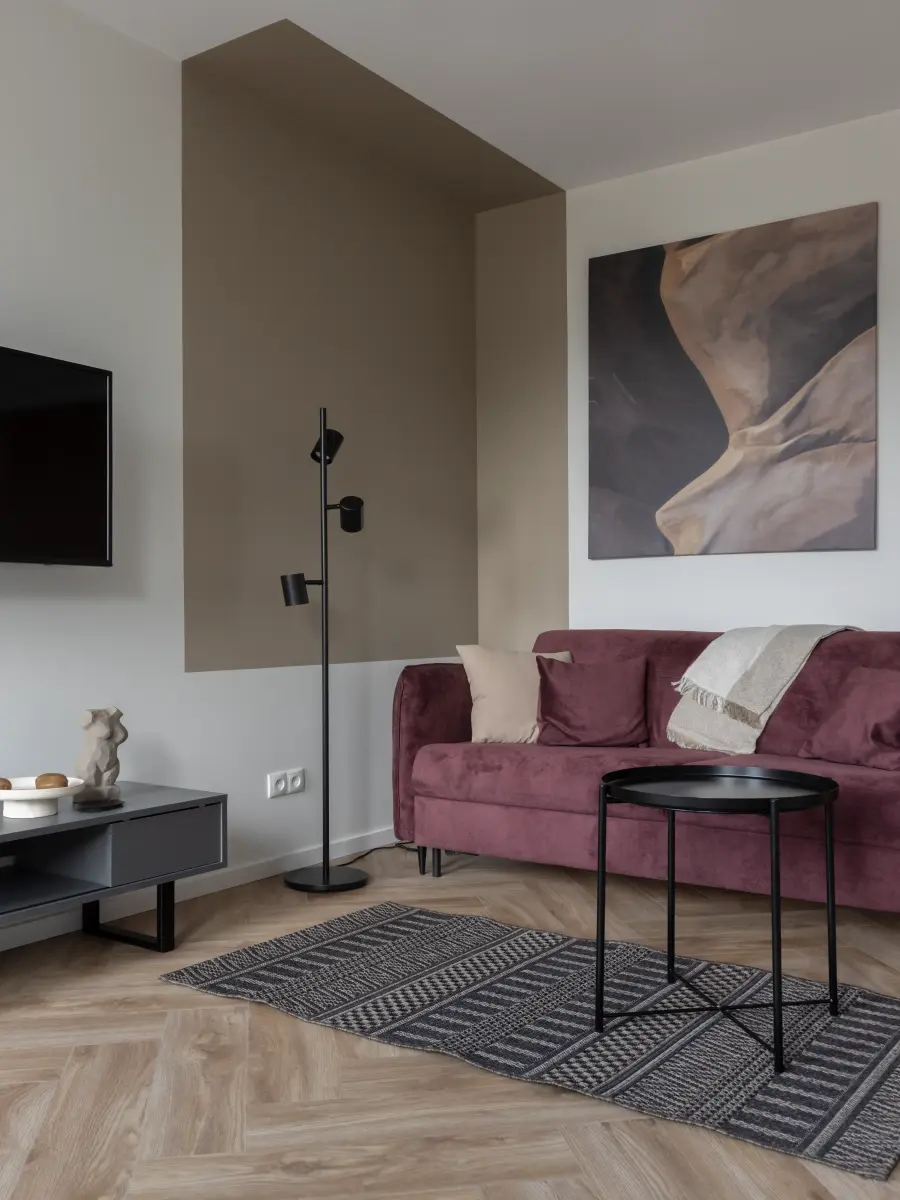 Weinrotes Sofa vor weiß-grauer Zimmerwand.