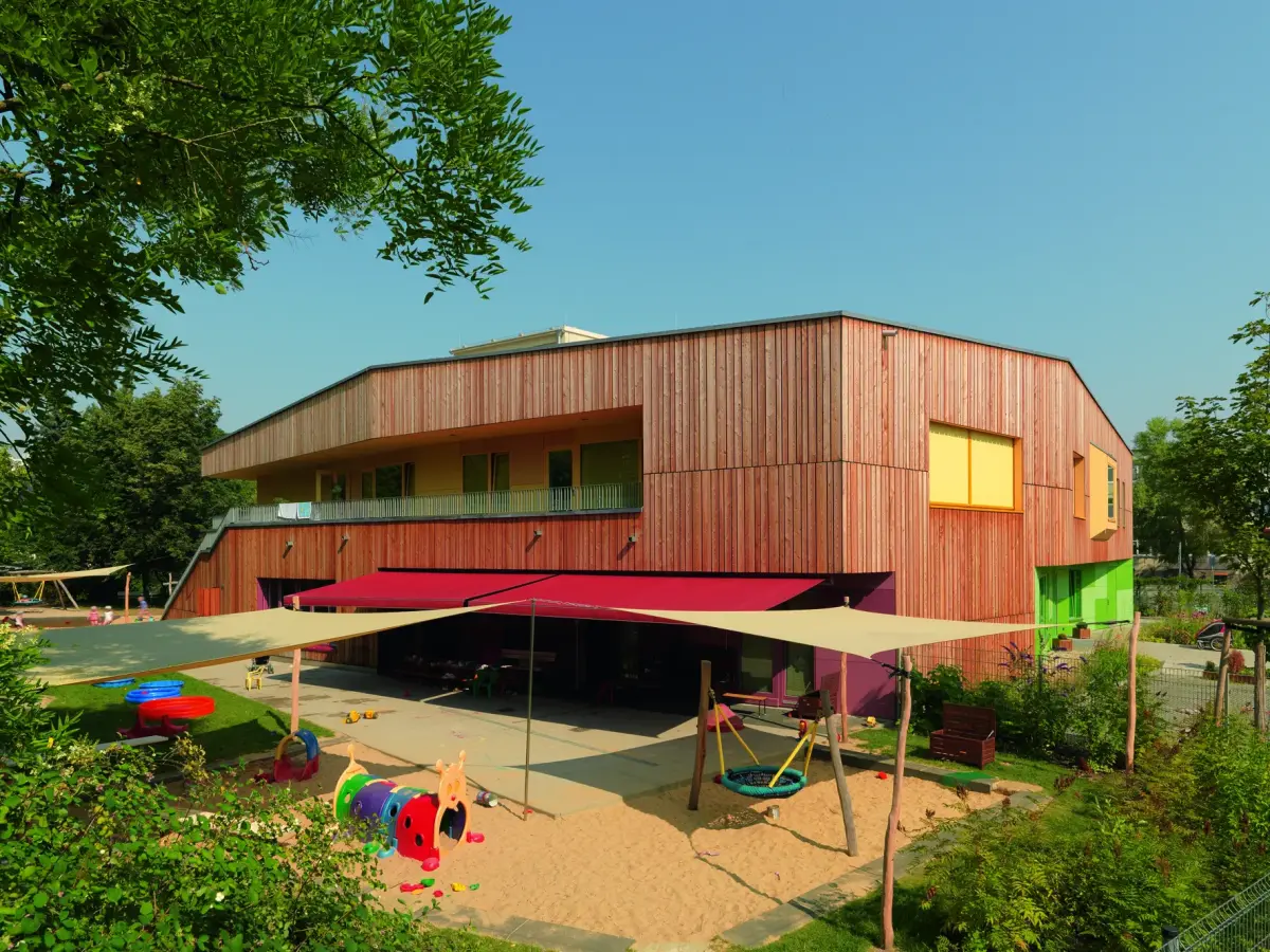 Blick auf den Spielplatz mit der Holzfassade im Hintergrund 