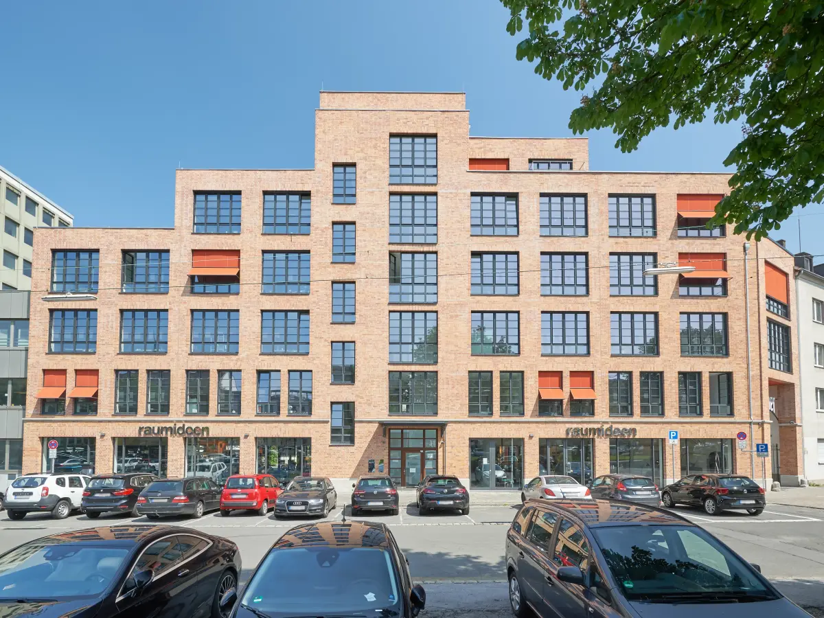 Blick vom Parkplatz auf das rote Backsteingebäude 