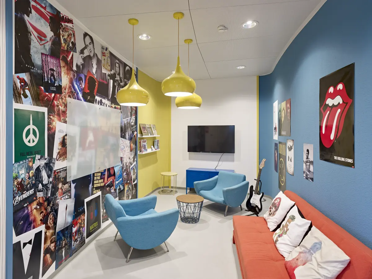 bunter Besprechungraum mit orangenem Sofa, gleben Lampen und blauer und bunter Bilder Wand