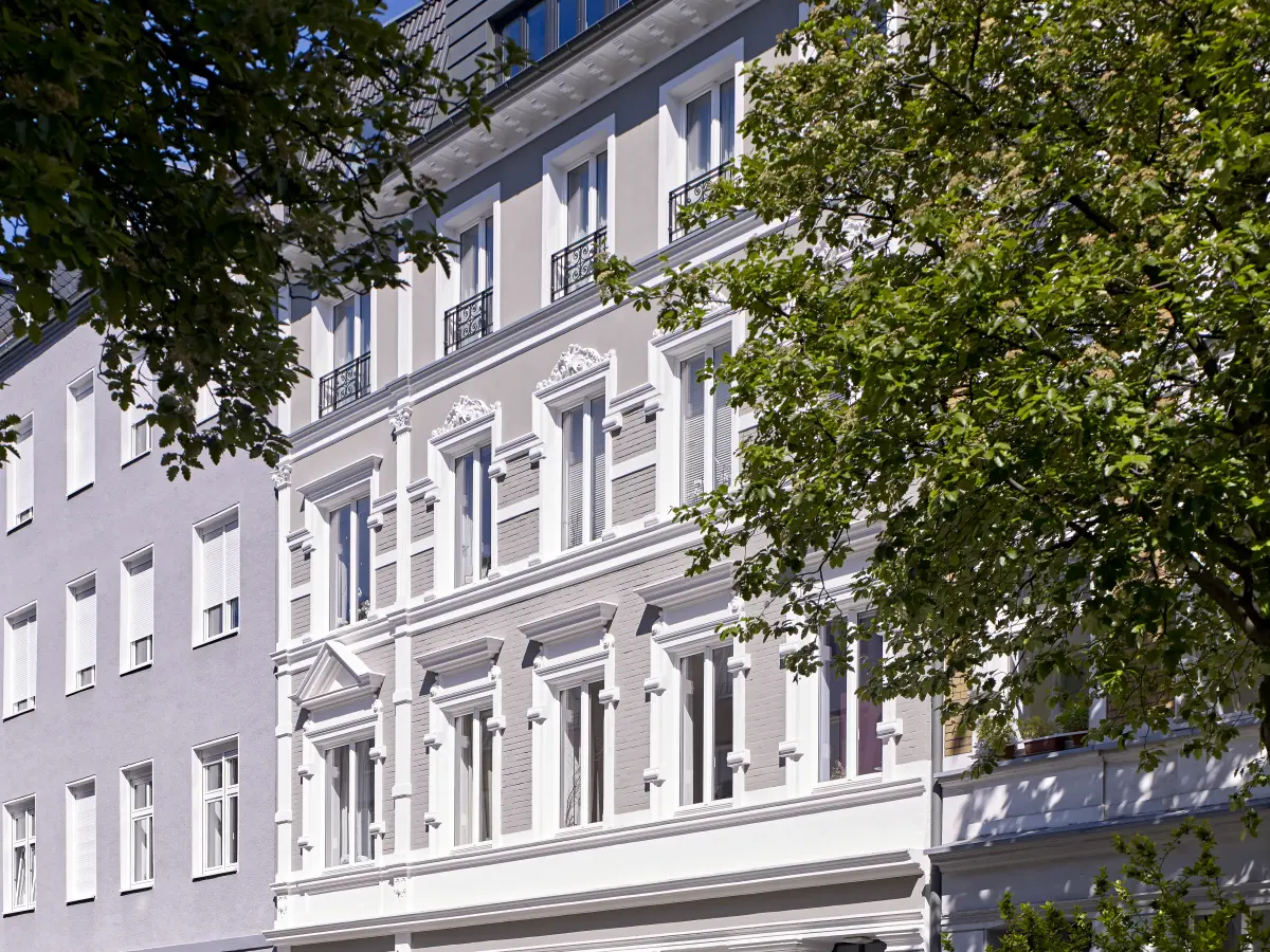 Blick durch die Bäume auf die Grau und Weiße Stilfassade 