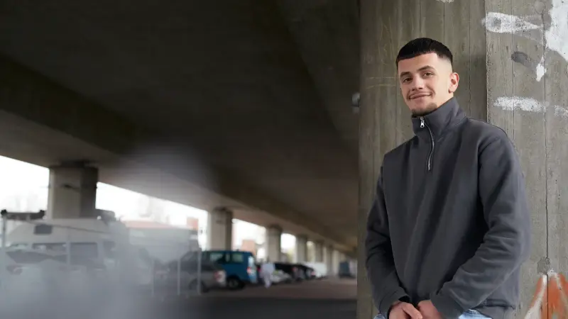 Ein junger mann im grauen Pullover schaut in die Kamera