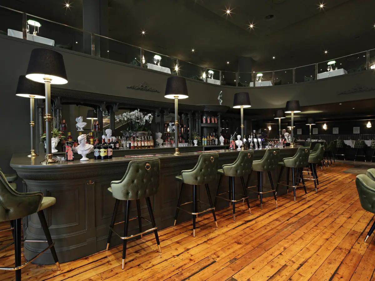 dunkles Interieur einer Bar mit Holzboden und grünen Sitzen