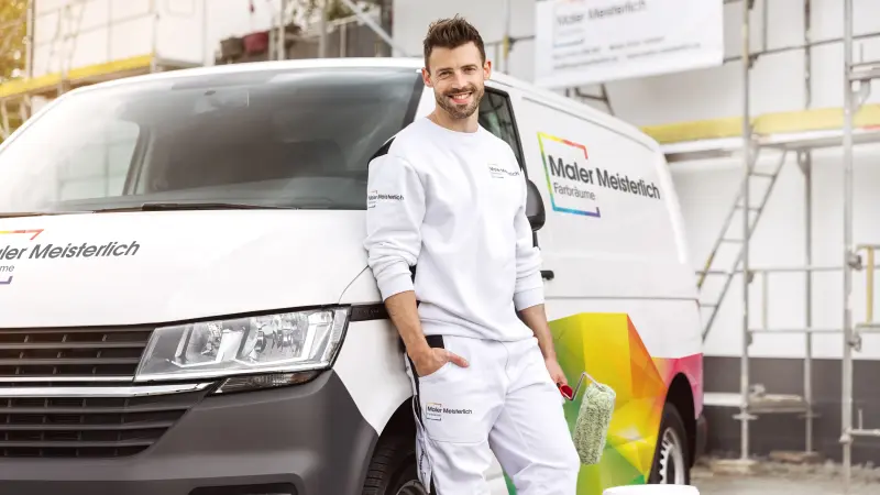 Mann lehnt an einem Firmenauto vor einer Baustelle