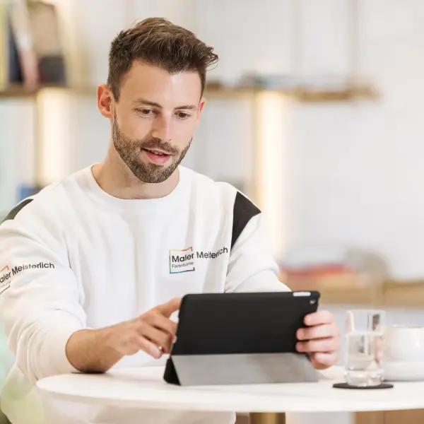 Mann sitzt am Tisch und schaut in sein Tablet