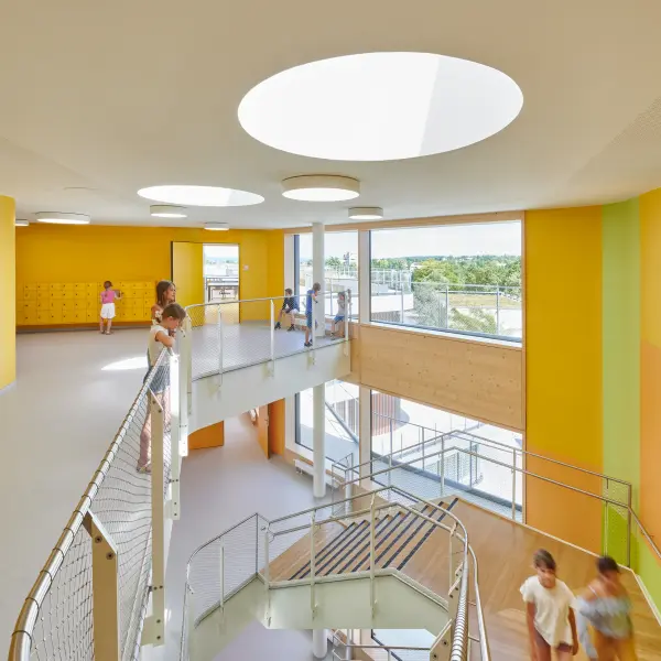 gelb und grün gestaltete Wände in einem Schulgebäude. Kinder stehen im Treppenhaus.