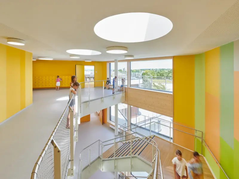gelb und grün gestaltete Wände in einem Schulgebäude. Kinder stehen im Treppenhaus.