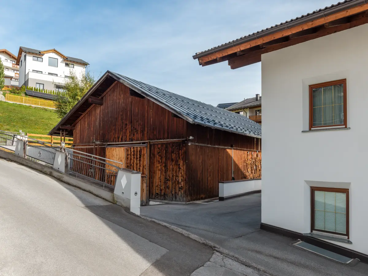 Traditionelles Holzgebäude neben modernem Wohnhaus in Fiss mit klarer Architektur.