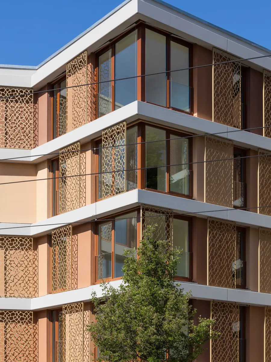 Dettaglio della facciata di un moderno edificio residenziale con finestre di grande formato, fasce marcapiano bianche ed elementi ornamentali in metallo.