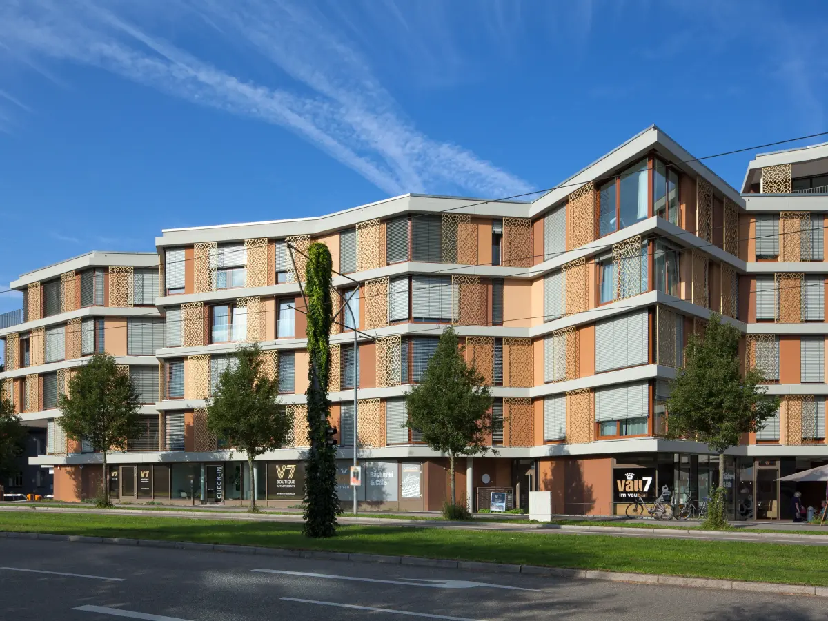 Moderno edificio residenziale e commerciale con facciata scandita ritmicamente, finestre a tutta altezza e superfici commerciali al piano terra.
