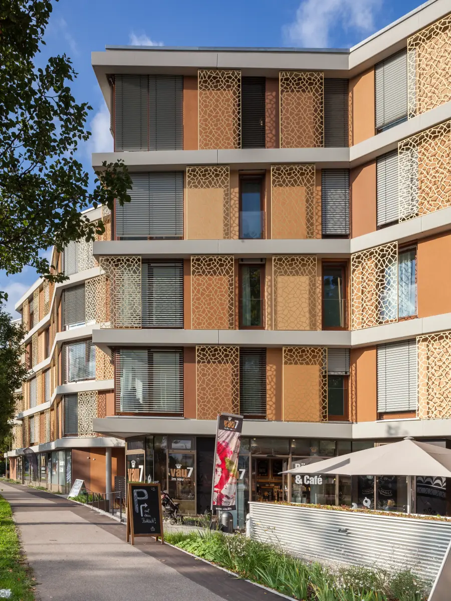 Edificio residenziale e commerciale a più piani con facciata articolata, pannelli metallici ornamentali e caffè al piano terra.