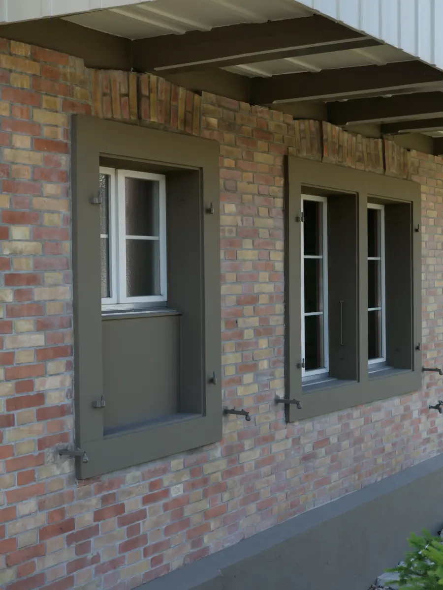 Detailansicht einer Fassade mit roten Klinkersteinen, grauen Fensterrahmen und geöffneten Fensterläden.
