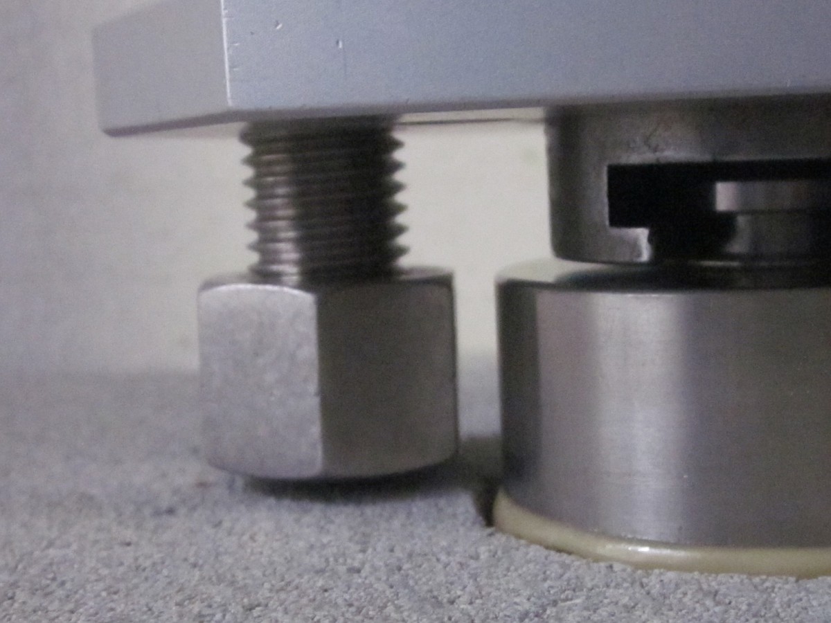 Nahaufnahme von zwei metallischen Füßen oder Maschinenschrauben auf einer Oberfläche.