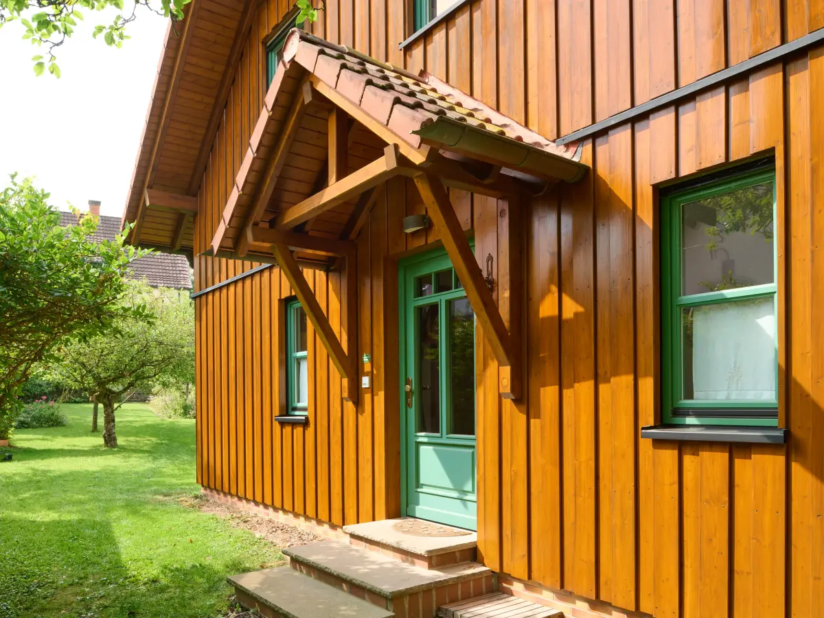 Großes dunkles Holzhaus mit grünen Fenster- und Türrahmen