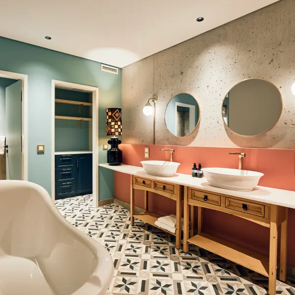  Ein modernes Badezimmer mit einem Doppelwaschbecken, runden Spiegeln, einer auffälligen rot-grauen Wand und türkisfarbenen Akzenten.