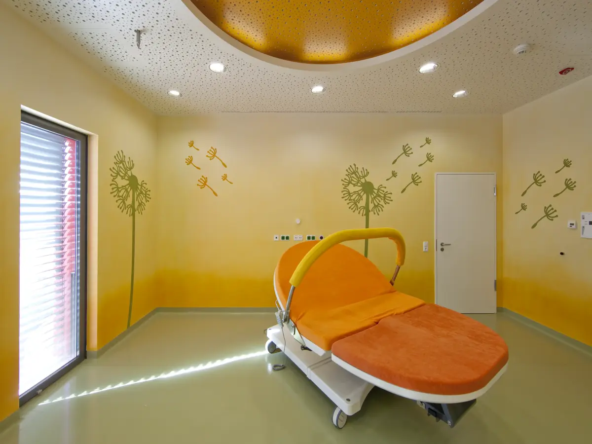 das Innere eines Krankenhauszimmers mit gelben Wänden und einem orangefarbenen Bett