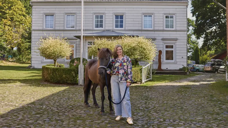 Eva steht mit ihrem Pony vor ihrem Haus