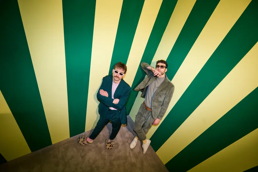 Christof und Michael stehen an einer gelb-grün-gestreiften Wand und schauen in die Kamera