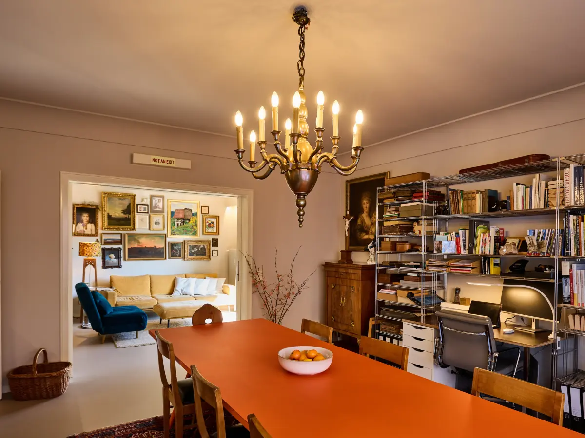 Essbereich mit orangefarbenem Esstisch und einem Bücherregal mit integriertem Arbeitsplatz dahinter. 