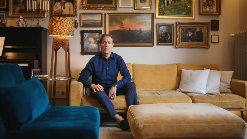 Jakob sitzt auf einem senfgelben Sofa und schaut mit ernstem Blick in die Kamera.